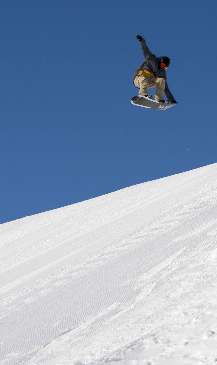 A snowboarder airborne high above a snow slope against a deep blue sky